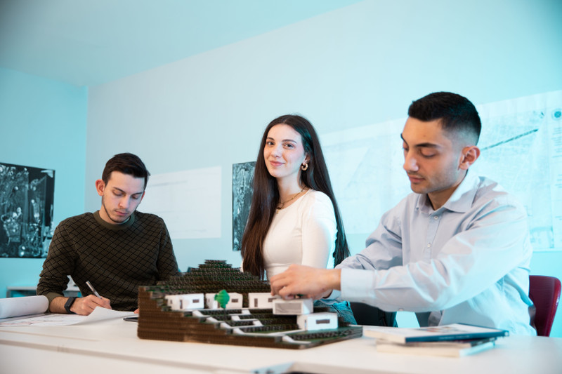 Three colleagues around a model at a table.