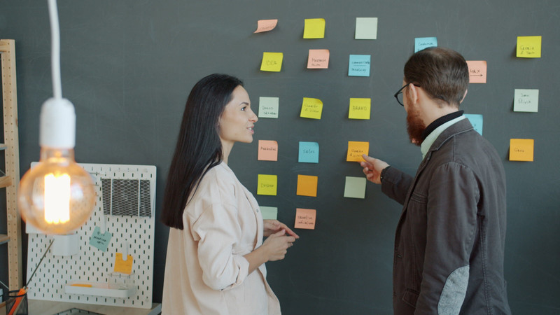 Two colleagues planning on a wall of coloured notes.